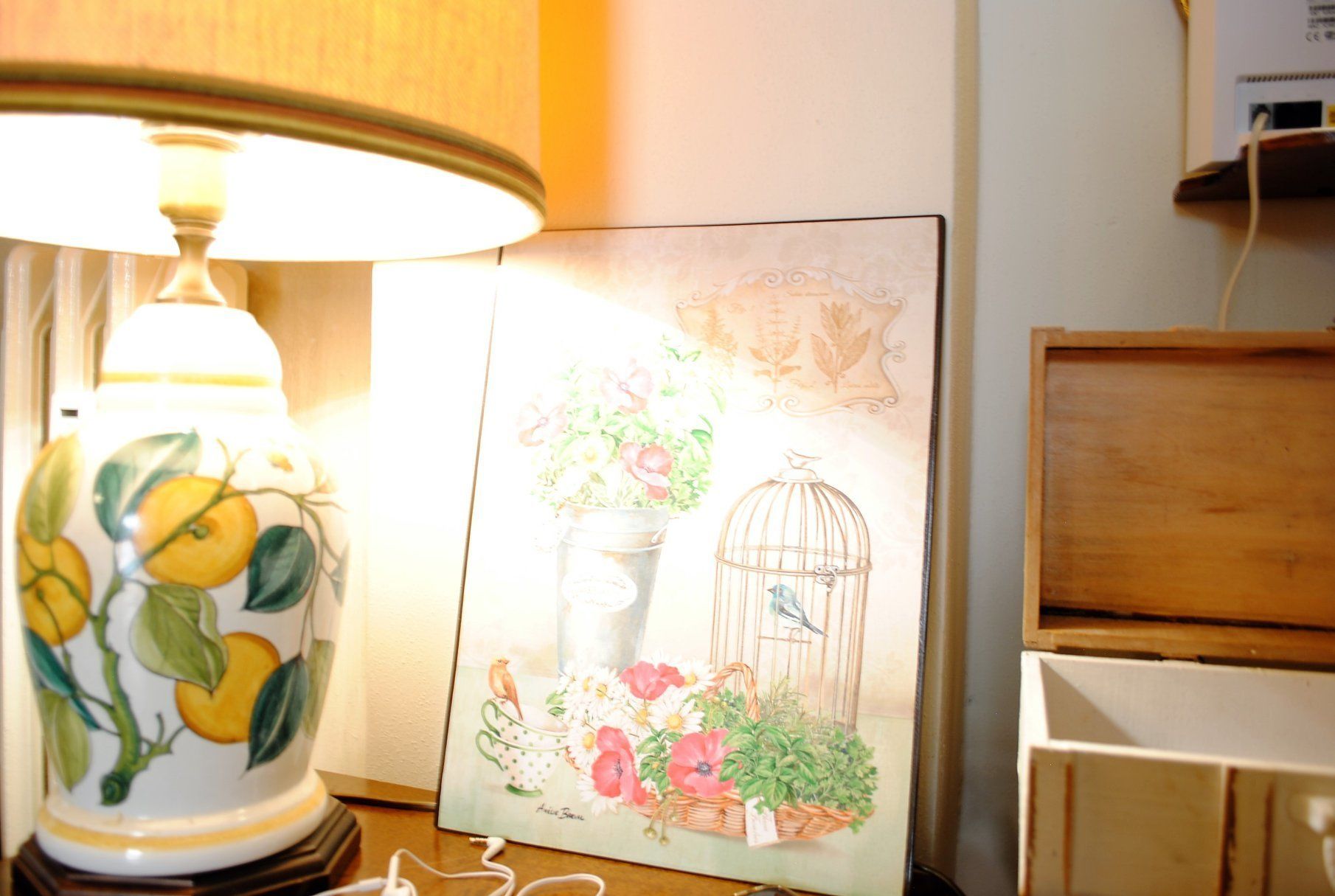 Una lampada con decorazioni floreali, un quadro incorniciato raffigurante uccelli e fiori, e una scatola di legno su un tavolo.