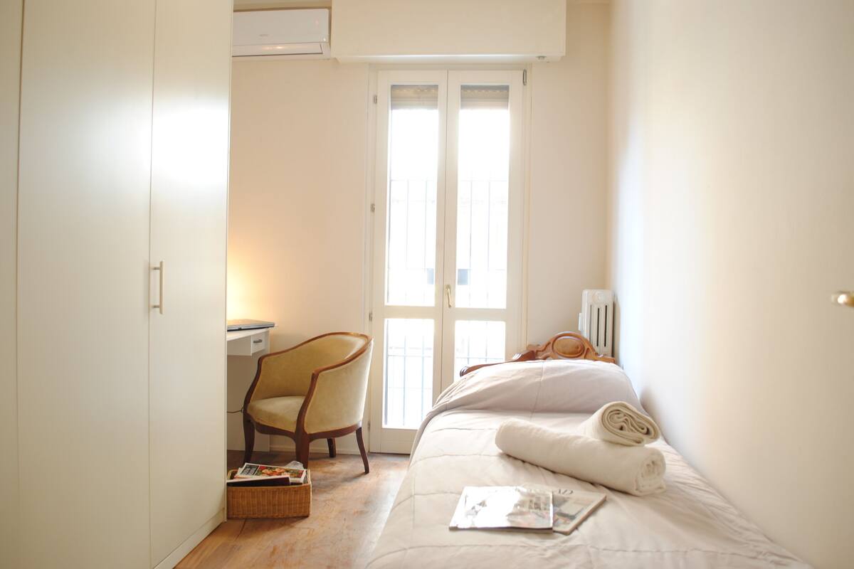 Een slaapkamer met een bed, een stoel, een bureau en een raam.