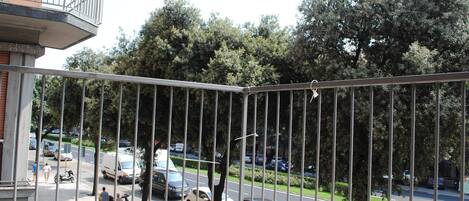 A balcony with a view of a busy street, trees, and parked cars.