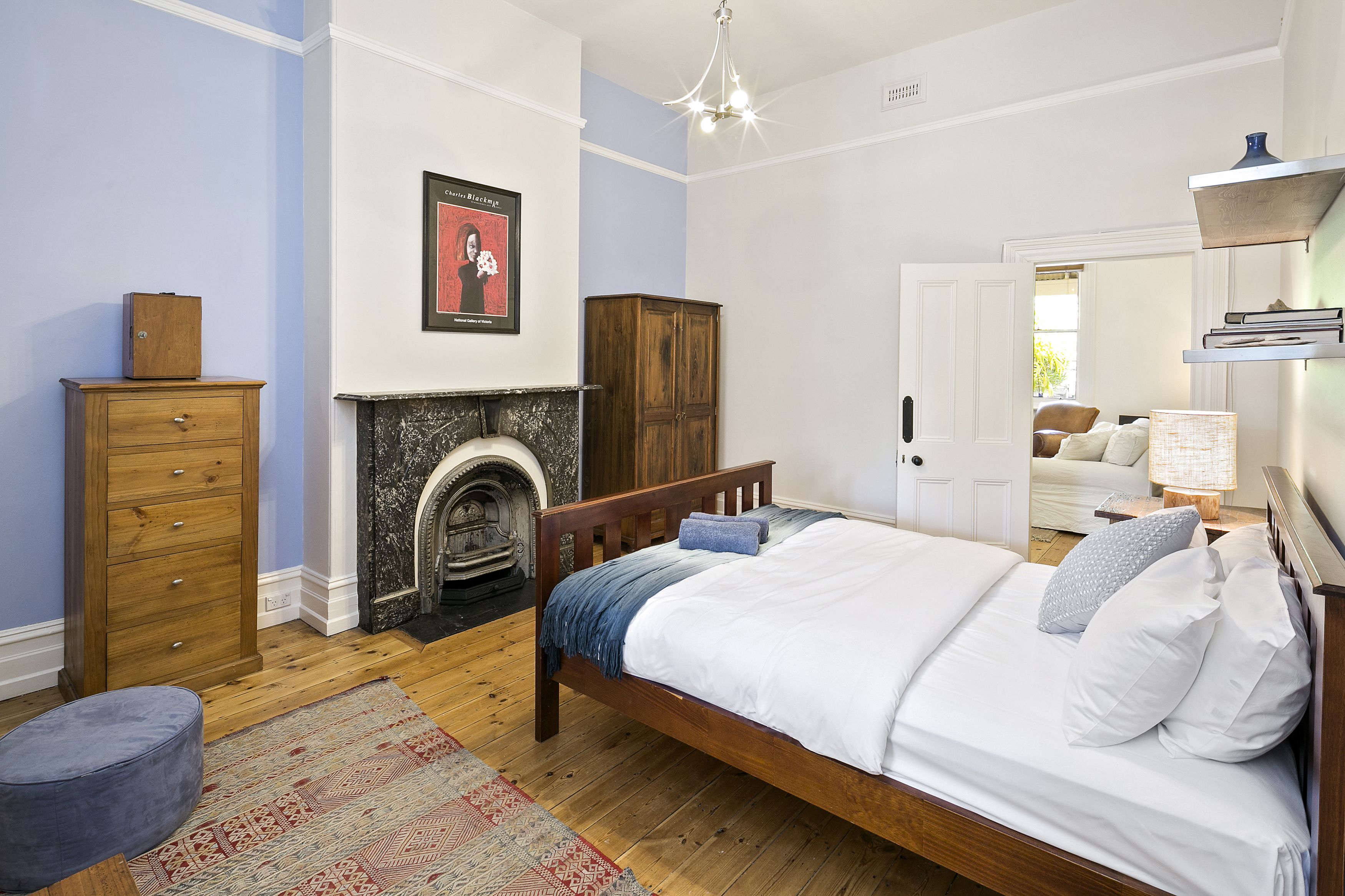 A bedroom with a wooden bed, a dresser, a fireplace, and a door leading to another room.