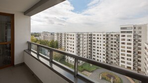 A balcony with a view of high-rise residential buildings, a clear sky, and a landscaped area below. - ShortStayPoland Krakowska - B65 (Warsaw)
