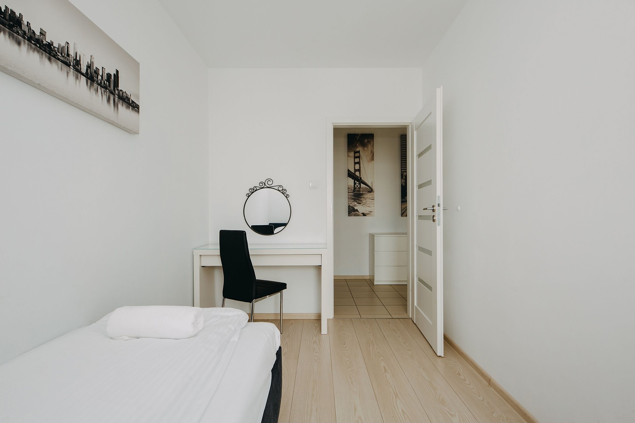 A bedroom with a bed, a desk, a chair, a mirror, and a door leading to a bathroom.