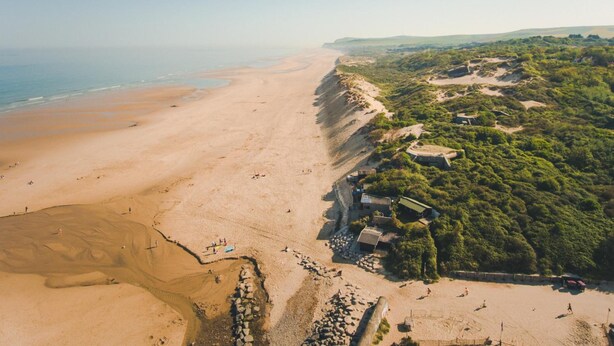 An aerial view of a beach with a sandy shore, a small building, and dense greenery. - Hôtel de la Baie de Wissant (Wissant)