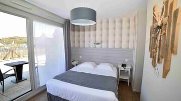 Un dormitorio con una cama grande, un ventanal corredero a un balcón y una lámpara colgante moderna.