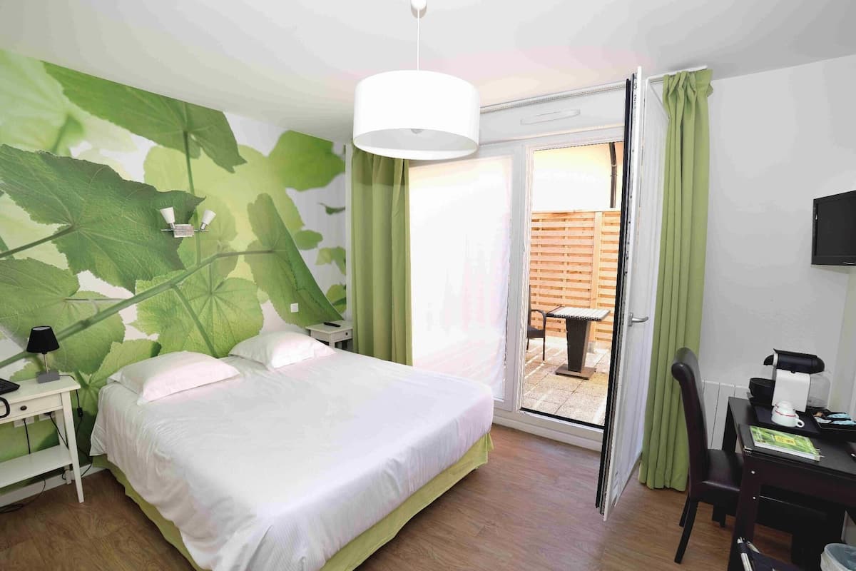 Ein Schlafzimmer mit einem Bett, einem Nachttisch, einem Schreibtisch, einem Stuhl, einem Fernseher und einer Glasgleittür, die zu einem Außenbereich führt.