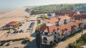 A coastal hotel with multiple buildings, a parking lot, and a beach in the background. - Hôtel de la Baie de Wissant (Wissant)