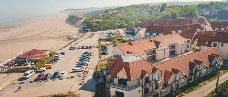 Un hôtel situé sur la côte, composé de plusieurs bâtiments, avec un parking et une plage en arrière-plan.