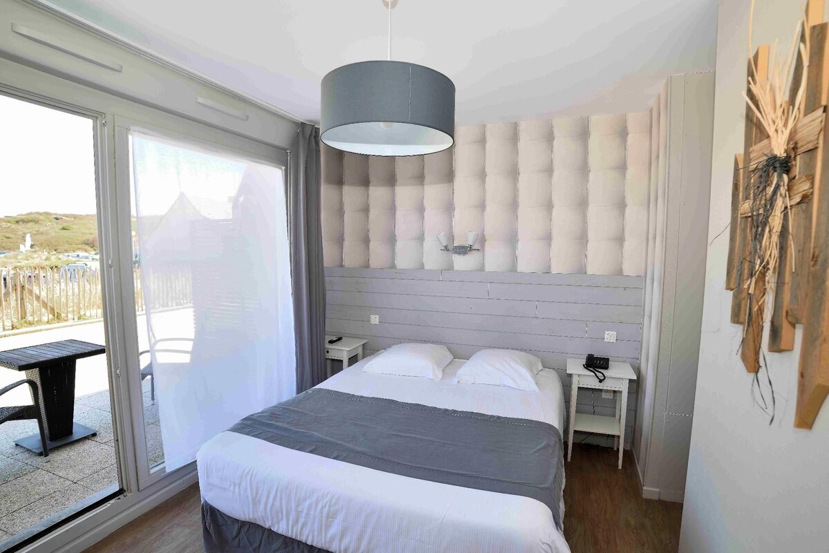 Une chambre à coucher avec un lit, une table de chevet, une lampe et une vue sur l’extérieur, accessible par une porte coulissante.