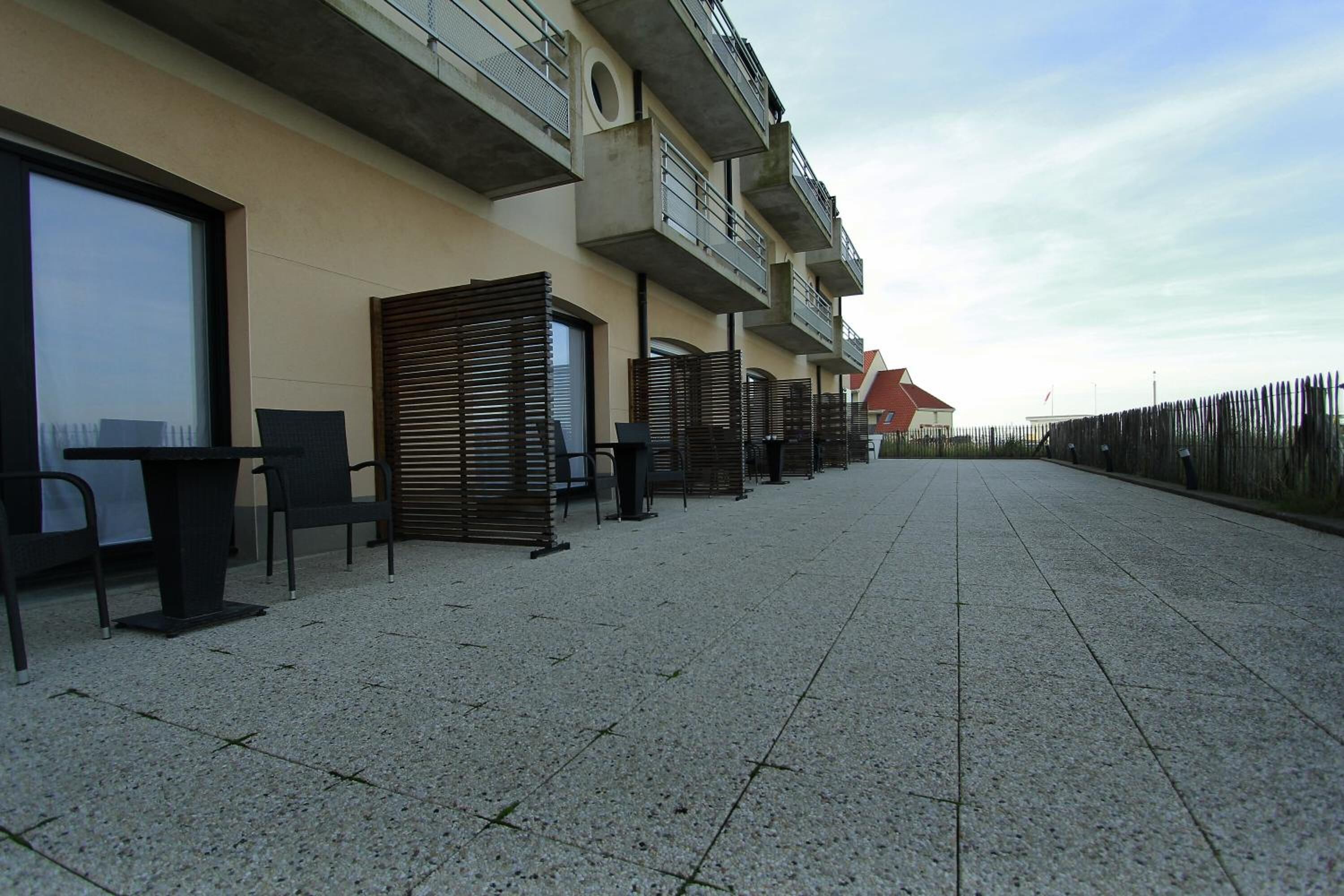 Un bâtiment dont le rez-de-chaussée est revêtu de carreaux, avec une rangée de sièges extérieurs et un balcon à l’étage supérieur.