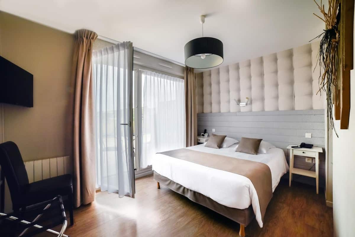 Ein modernes Hotelzimmer mit einem großen Bett, einem Schreibtisch, einem Sessel und einem an der Wand montierten Fernseher.