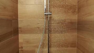 Een douche met een regenkop, een handdouche en een bedieningspaneel aan de muur.