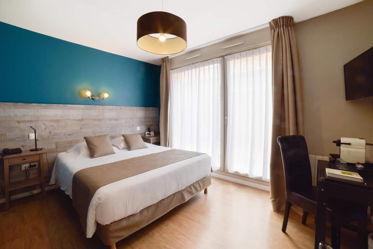 Ein Hotelzimmer mit Bett, Nachttischen, Schreibtisch, Stuhl, Fernseher und einem großen Fenster mit Vorhängen.