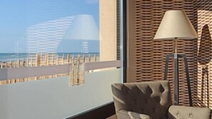 A room with a large window offering a view of the beach and ocean. There is a chair and a floor lamp near the window. - Hôtel de la Baie de Wissant (Wissant)