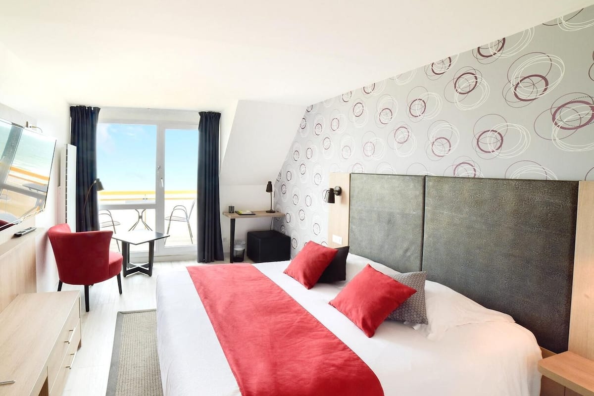 Ein Hotelzimmer mit Bett, Schreibtisch, Stuhl, Fernseher und Meerblick.