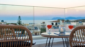 A balcony with wicker chairs, a round table, two glasses of red drink, and a decorative glass on the table.