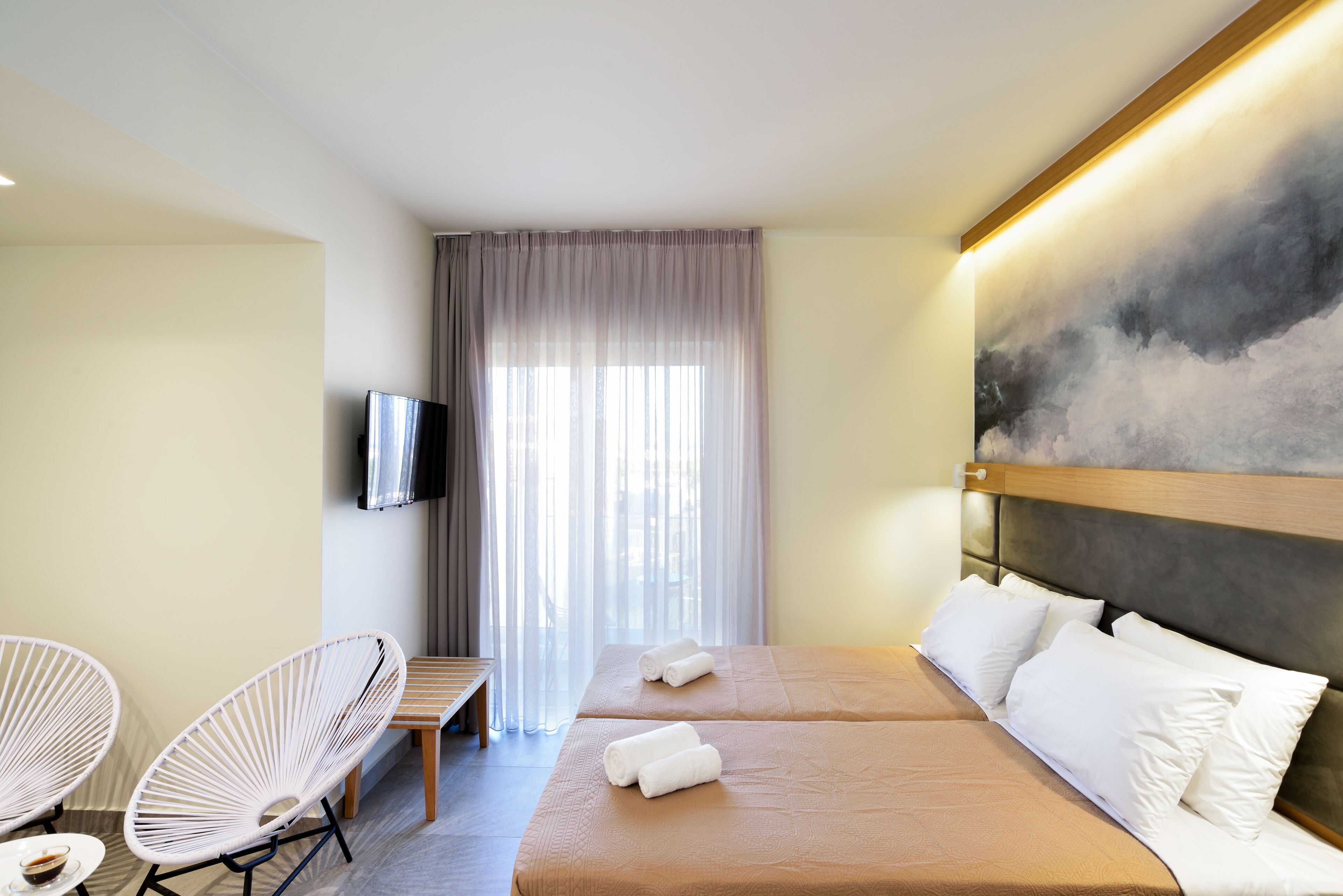 A hotel room with two beds, a TV, a painting, and a window with curtains.