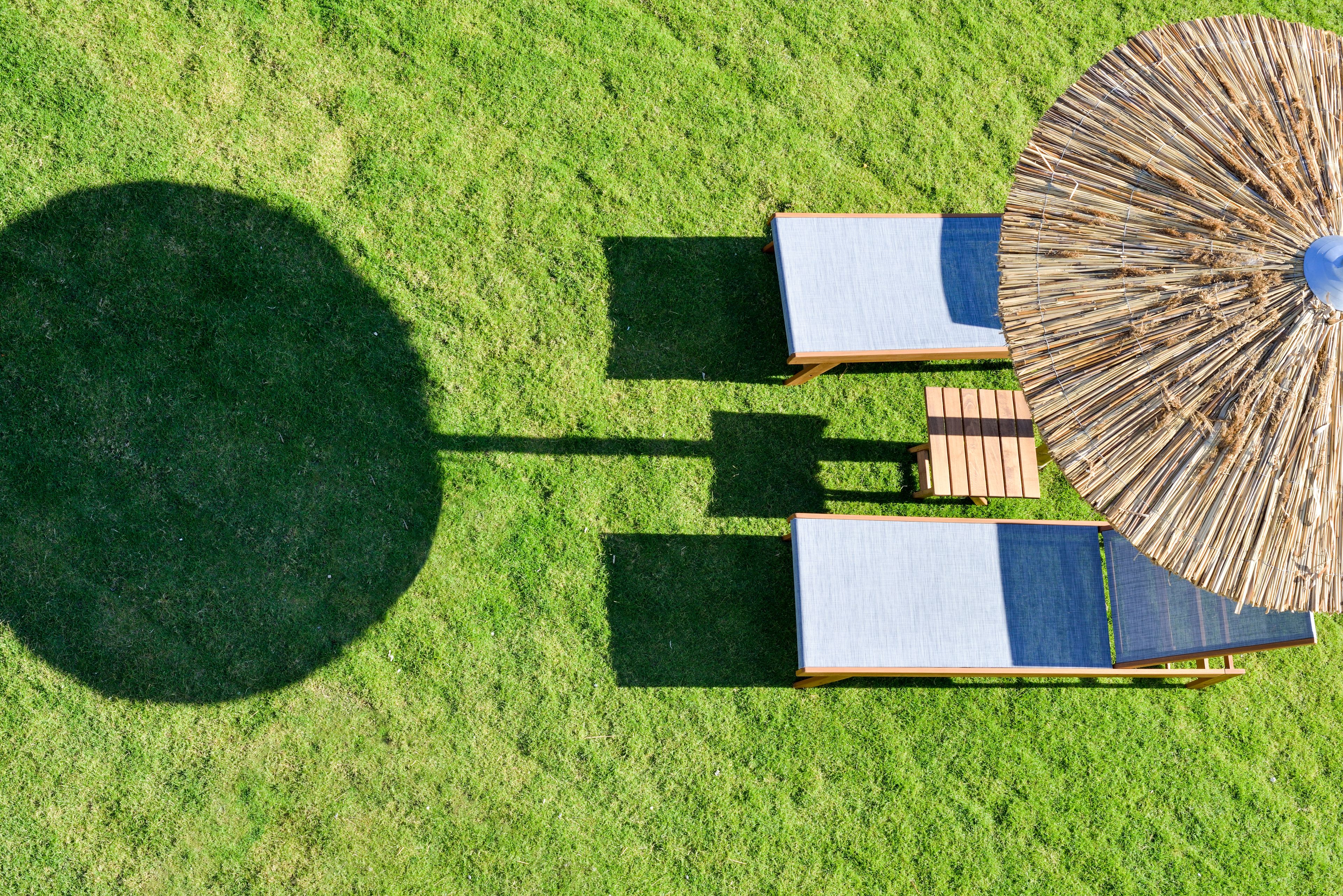 An aerial view of a grassy area with two lounge chairs and a large woven umbrella.