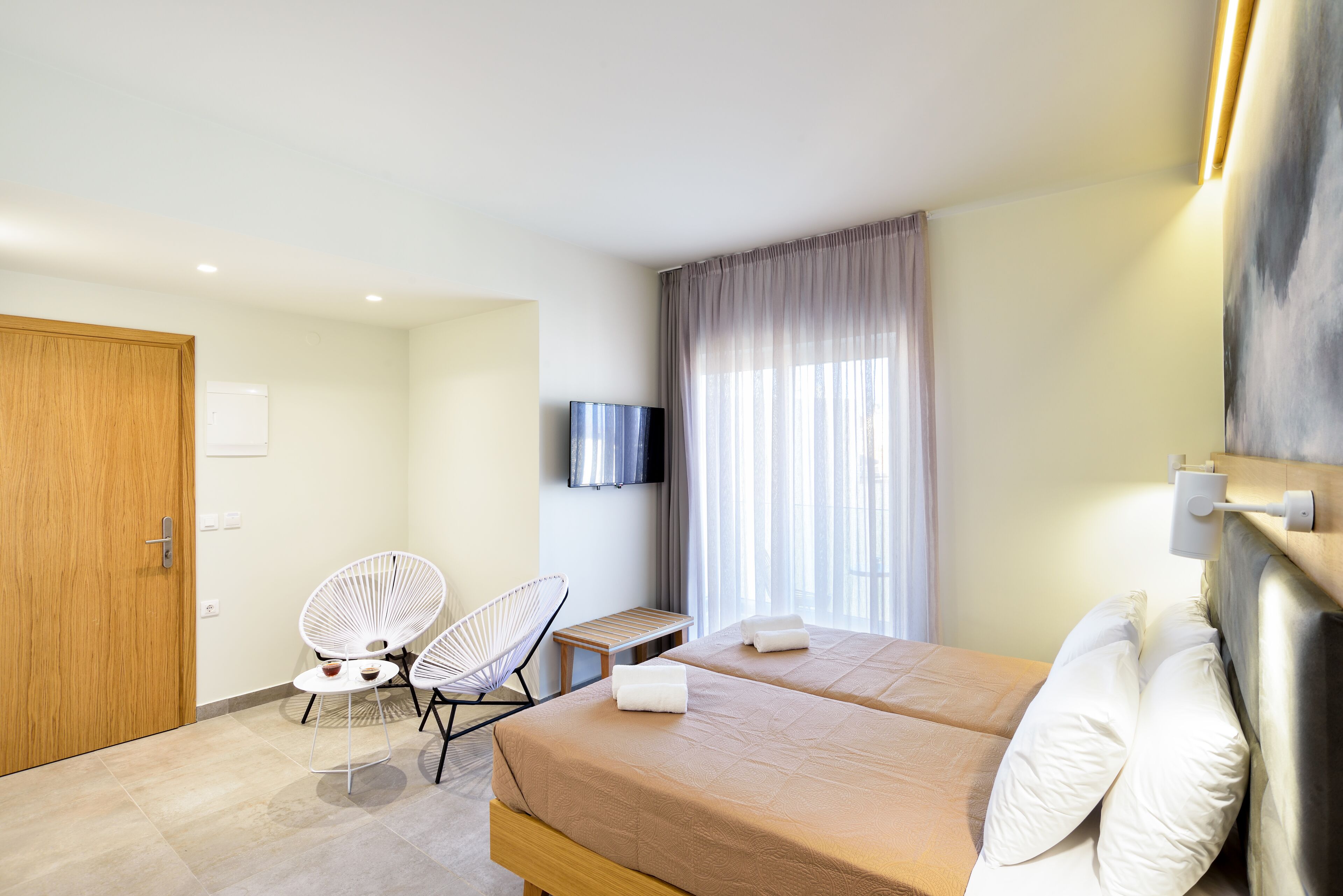 Une chambre d’hôtel avec deux lits, une télévision, une porte en bois et une fenêtre avec des rideaux.