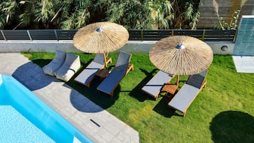 Een zwembadgedeelte met ligbedden en twee rieten parasols.
