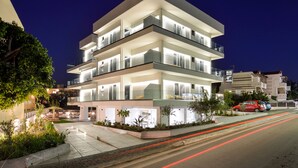 A multi-story modern building with balconies, a well-lit entrance, and a landscaped outdoor area.