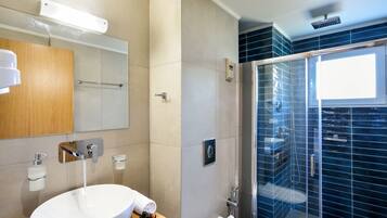 A modern bathroom with a large sink, mirror, towel rack, and a glass-enclosed shower area.