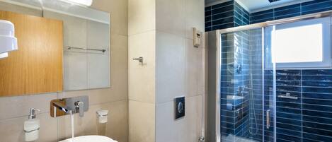 A modern bathroom with a large sink, mirror, towel rack, and a glass-enclosed shower area.