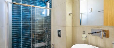 A modern bathroom with a glass shower enclosure, a white sink, and a wooden vanity.