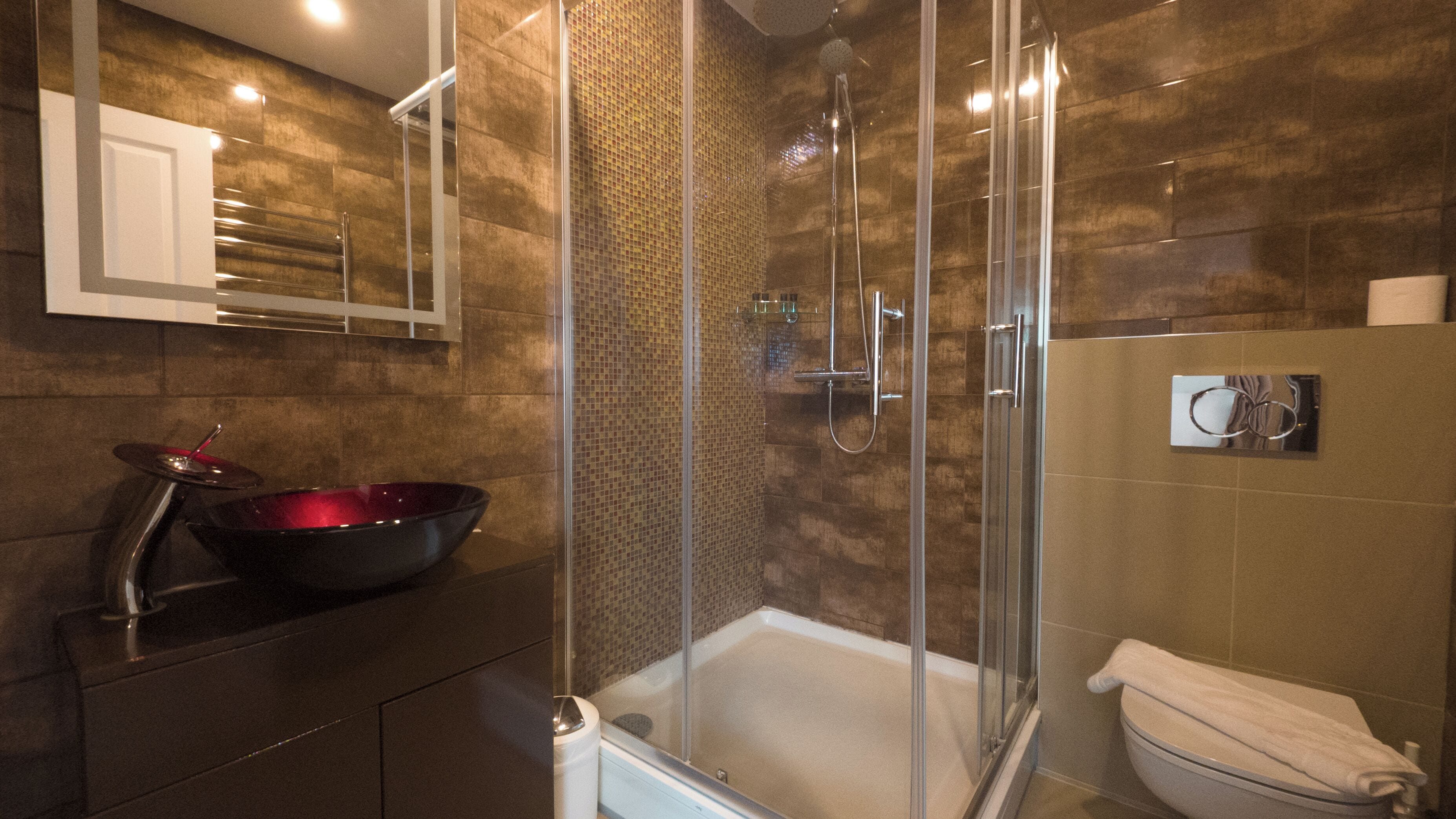 A modern bathroom with a glass-enclosed shower, a large black vessel sink, and a white toilet.