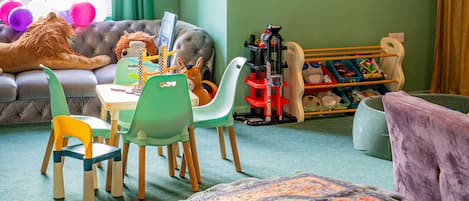A children's playroom with a large window, green walls, and a variety of toys and furniture.