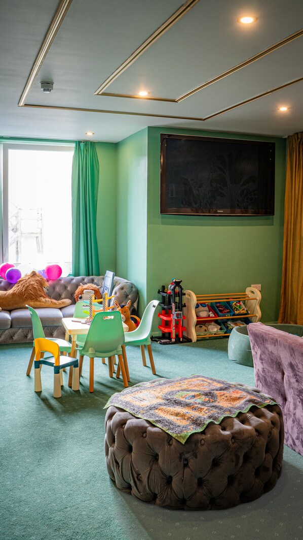A children's playroom with a large window, green walls, and a variety of toys and furniture.