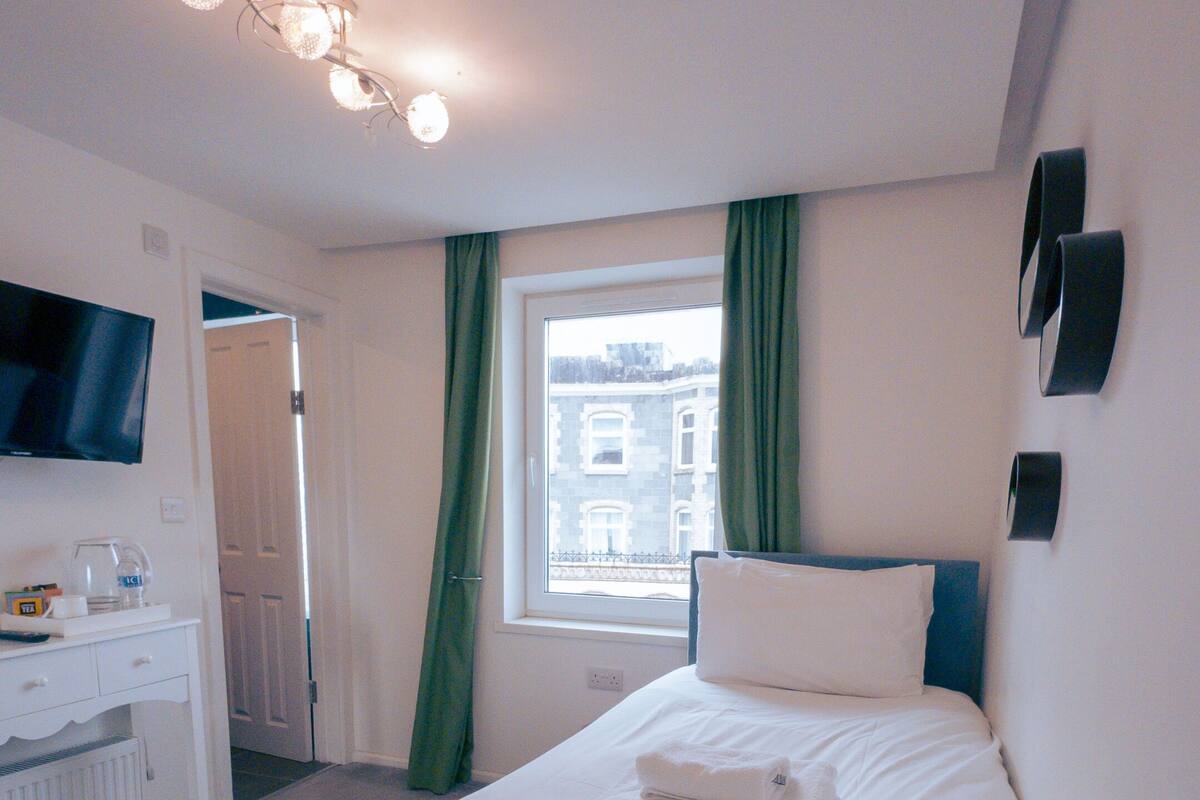 Ein ordentlich eingerichtetes Hotelzimmer mit einem Bett, einem Schreibtisch, einem Fernseher und einem Fenster mit Vorhängen.