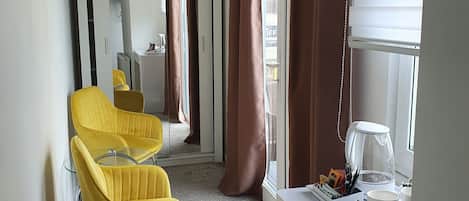 A hotel room with a desk, two yellow chairs, a coffee maker, and a trash bin.