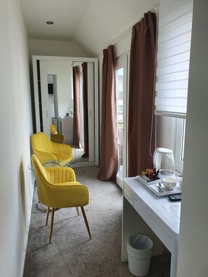 A hotel room with a desk, two yellow chairs, a coffee maker, and a trash bin.