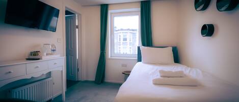 Habitación de hotel con cama, escritorio con televisor de pantalla plana, ventana con cortinas y radiador.