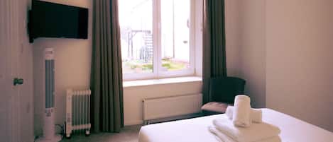A hotel room with a bed, a flat-screen TV, a window with curtains, a radiator, and a wall-mounted heater.