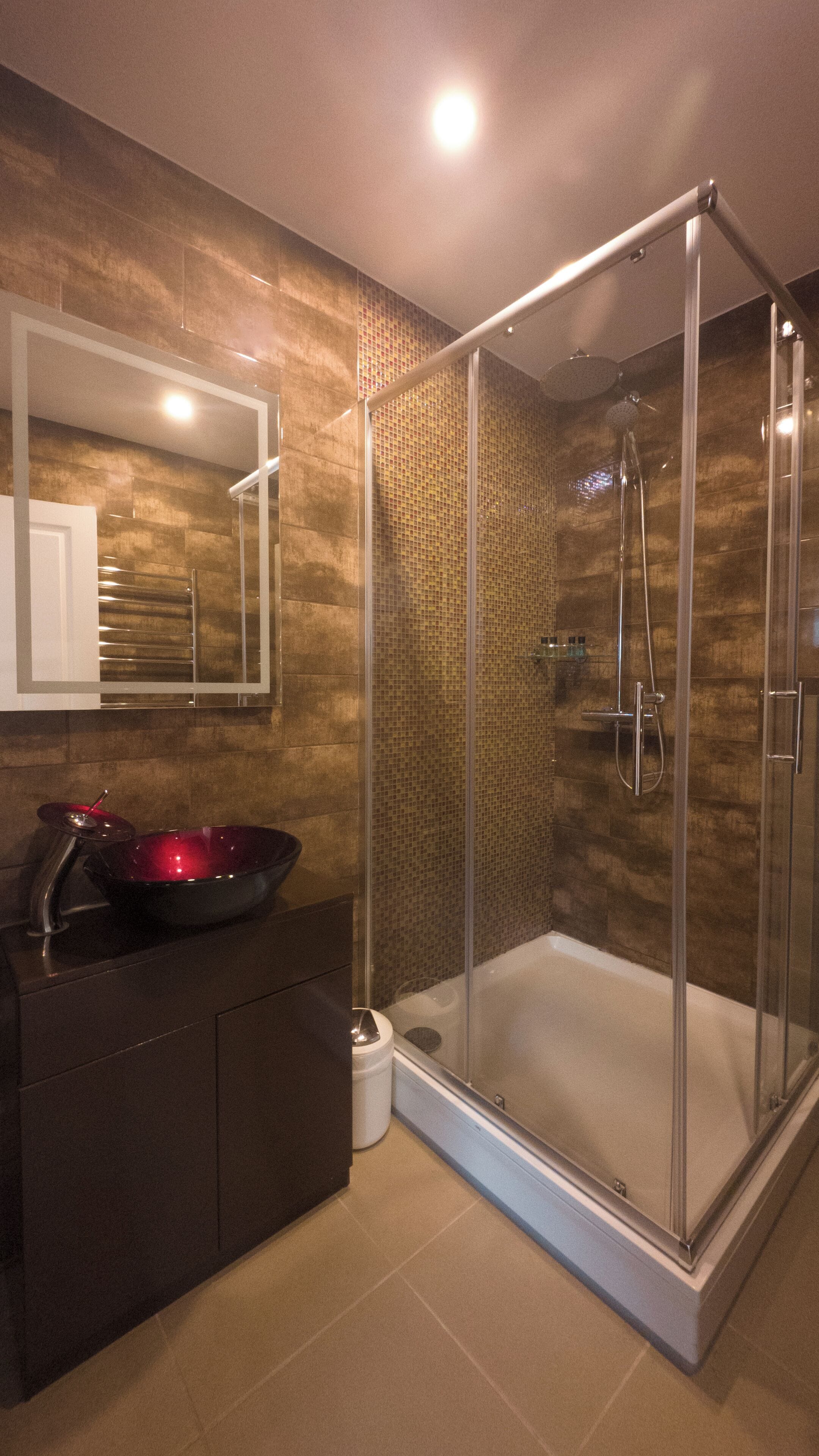A modern bathroom with a glass-enclosed shower, a large mirror, and a dark-toned vanity.