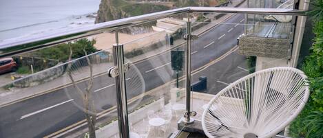 A balcony with a glass railing overlooking a coastal road and beach.