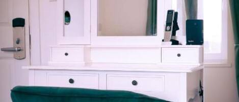 Une coiffeuse blanche avec un grand miroir, une chaise verte à revêtement en tissu et une fenêtre avec des rideaux.