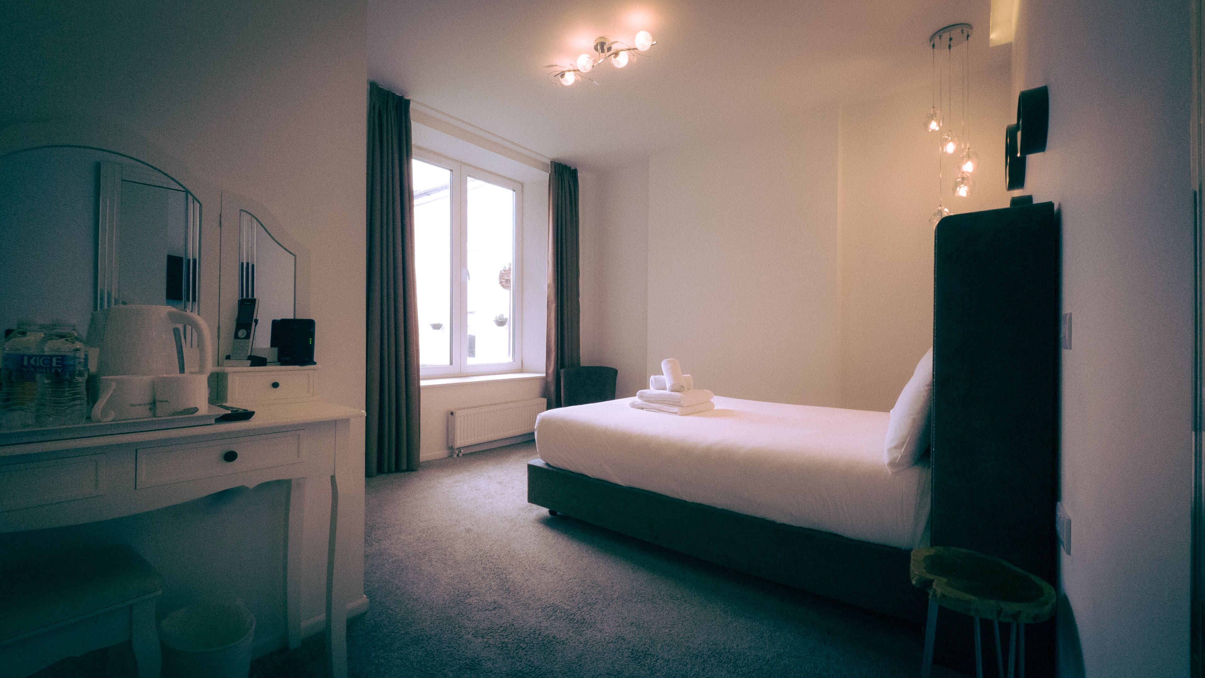 A hotel room with a bed, a desk, a chair, a mirror, and a window with curtains.