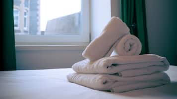 A neatly made bed with folded towels and a window with curtains.