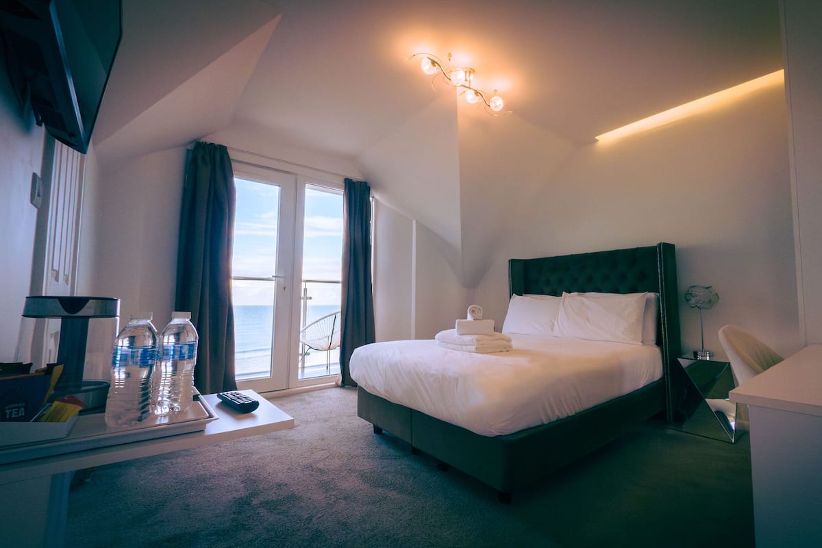 Ein Hotelzimmer mit Bett, Schreibtisch mit Computer, Stuhl, Fenster mit Vorhängen und Blick aufs Meer.