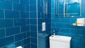 A bathroom with blue tiles, a white toilet, a sink, a mirror, and a toilet paper holder.