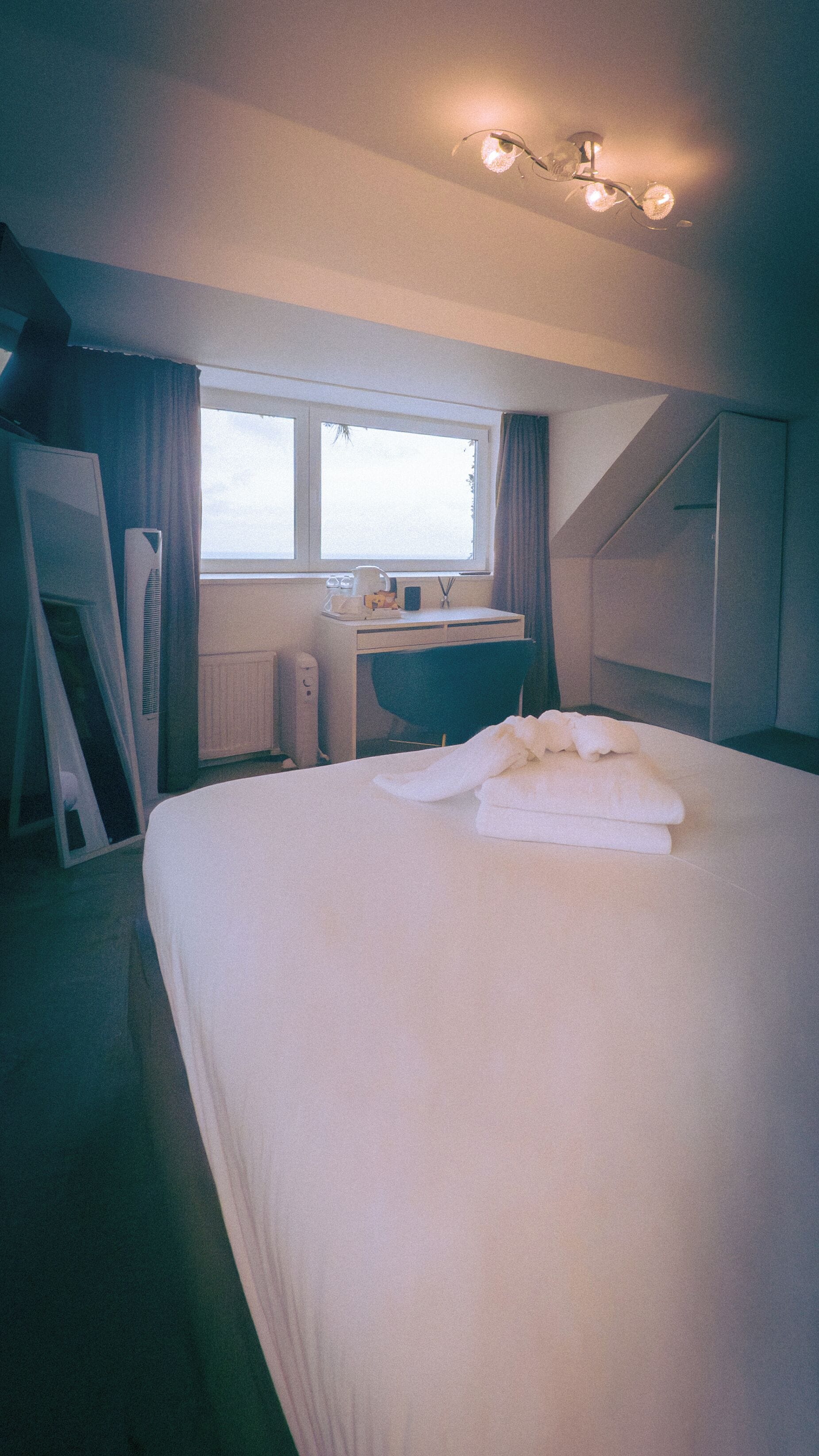 A hotel room with a large bed, a desk, a chair, a window, and a radiator.
