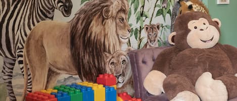 A room with a lion and zebra mural, a plush monkey, and a ball pit.