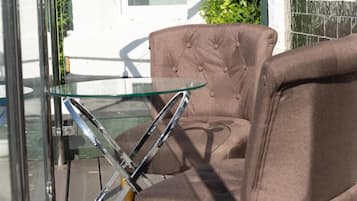 Una silla marrón con tapizado y una mesa de vidrio frente a una pared blanca y una ventana.