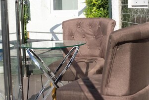 Una silla marrón con tapizado y una mesa de vidrio frente a una pared blanca y una ventana.