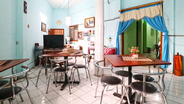 Uma área de refeições com televisão, mesas, cadeiras e uma cozinha ao fundo.
