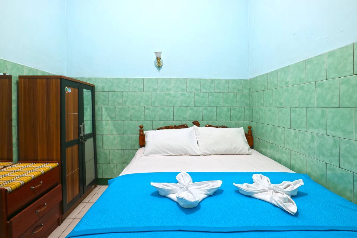 A hotel room with a bed, a wooden wardrobe, and a green tiled wall.