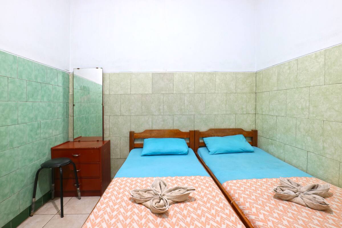 A small, clean room with two beds, a wooden dresser, and a stool.