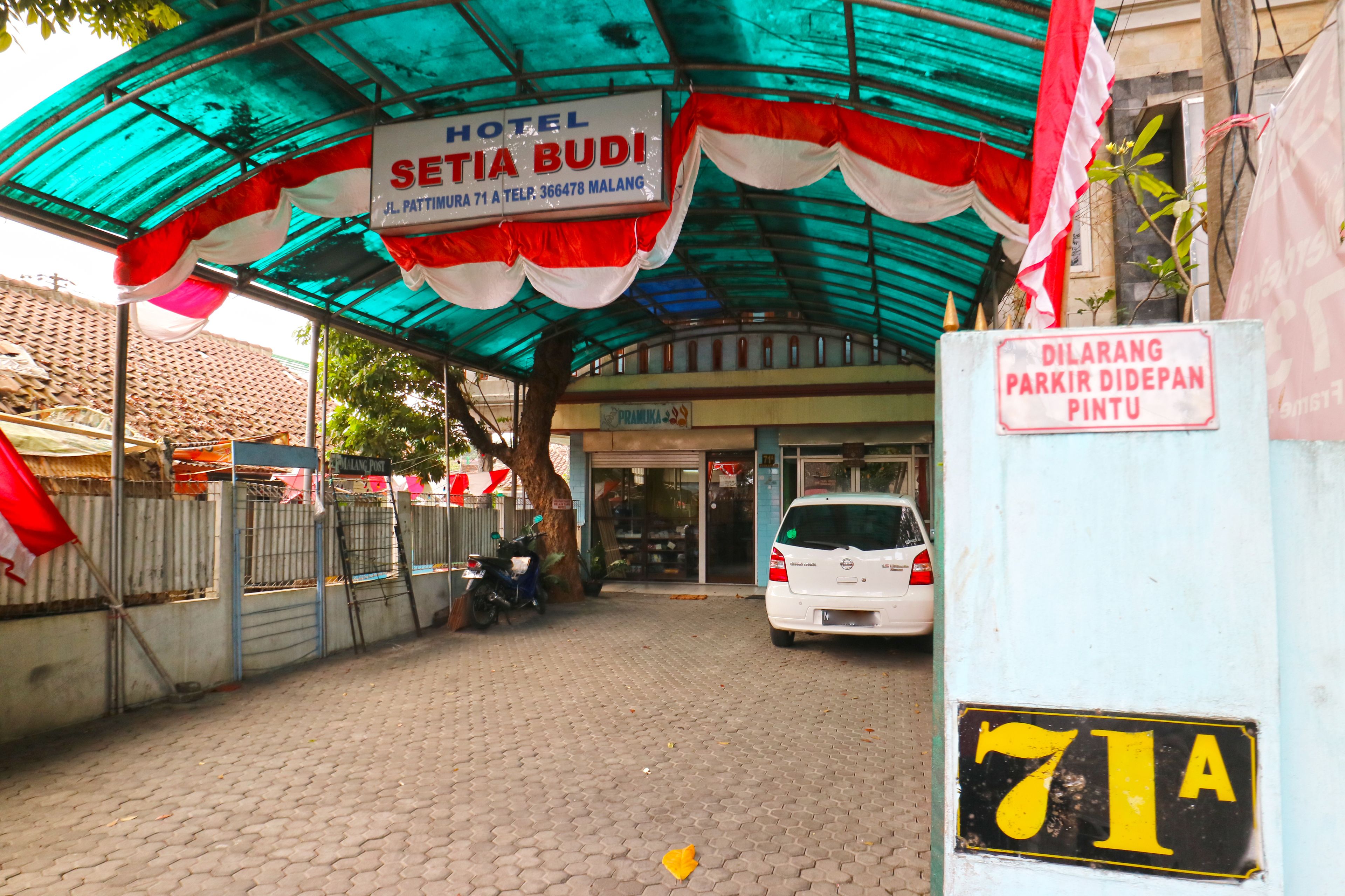 A hotel entrance with a sign for Hotel Setia Budi, a parked car, and a sign indicating parking availability.